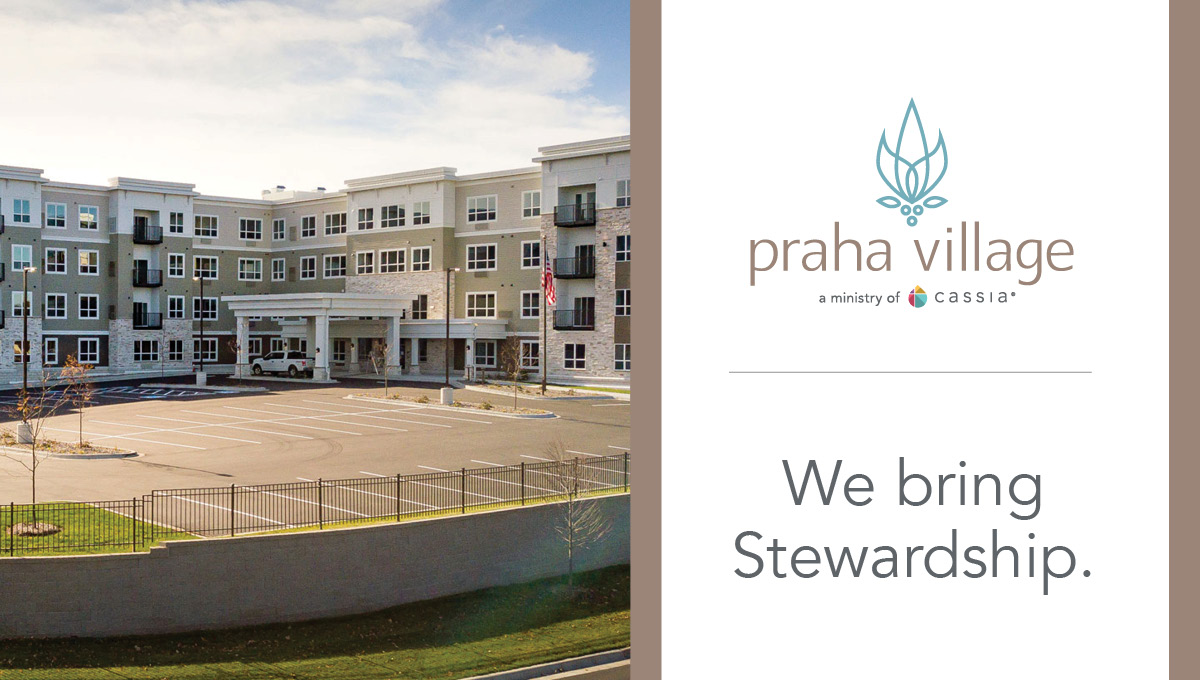 Exterior view of Praha Village senior living community featuring a modern multi-story building, covered entrance, parking lot, and landscaped grounds in New Prague, Minnesota.